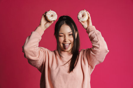 Happy young woman posing holding donuts over pink wall background
