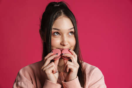 Asian brunette happy woman smiling while posing with macaroons isolated over purple wall