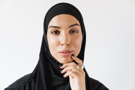 A portrait of a pensive muslim woman with pierced nose holding a hand near the face in the white...