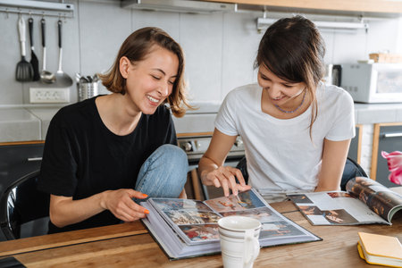 A portrait of the smiling lesbian couple looking at the photos in the album in the light kitchenの写真素材