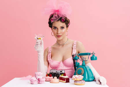 Young woman in pink dress calling on landline phone while sitting at the table over isolated...