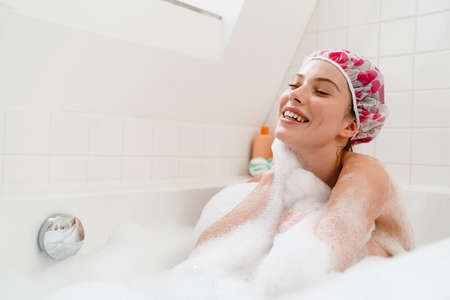 Young white smiling woman relaxing in a bubble bath, wearing shower capの写真素材