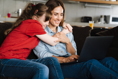 Woman and her daughter with down syndrome using laptop while sitting on sofa at home