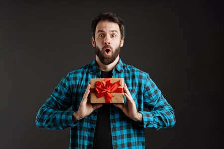 Bearded surprised white man exclaiming while showing gift box isolated over black backgroundの写真素材