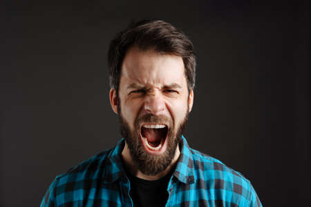 Bearded white angry man screaming and looking at camera isolated over black backgroundの写真素材