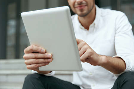 Close up of businessman sitting on stairs and using digital tablet. Obscure face of smiling young...