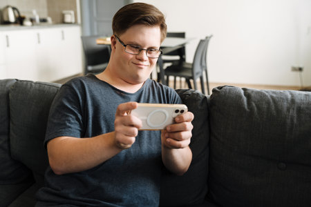 Young man with down syndrome using cellphone while sitting on couch at home