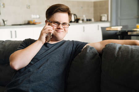 Young man with down syndrome talking on cellphone while sitting at homeの写真素材