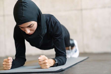 Young muslim sportswoman in hijab doing exercise while working out indoorsの写真素材