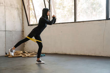 Young muslim woman in hijab unrolling fitness mat indoors