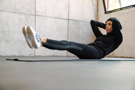 Young muslim sportswoman in hijab doing exercise while working out indoors
