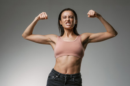 White woman wearing brassiere grimacing while showing her biceps isolated over grey backgroundの写真素材