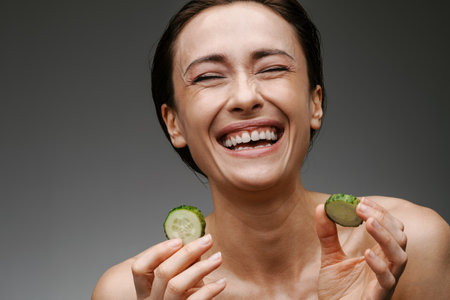White shirtless woman laughing while posing with cucumber isolated over grey backgroundの写真素材
