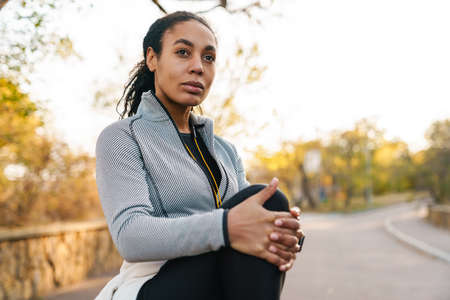 Focused african american sportswoman stretching her leg while working out in park