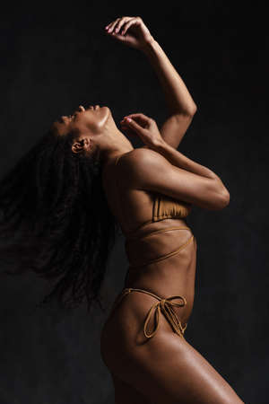 Black brunette woman in swimsuit posing on camera isolated over black backgroundの写真素材