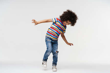 Happy preschooler african boy standing on one leg over white wall, having fun, full length