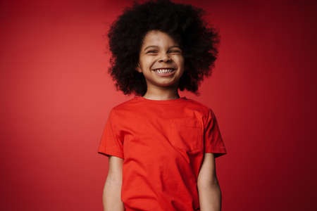 Smiling little african boy in everyday clothes over red wall backgroundの写真素材