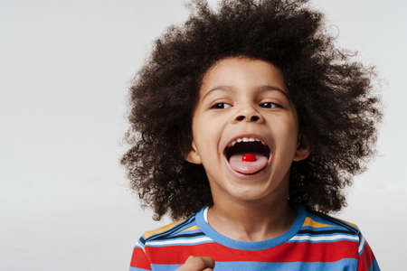 Close up of a happy preschooler african boy wearing t-shirt over white wall, sticking his tongue out...