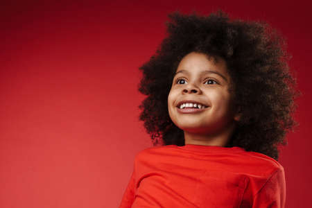 Smiling little african boy in everyday clothes over red wall background, looking away, close upの写真素材