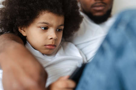 Black father and son using tablet computer while resting together at homeの写真素材