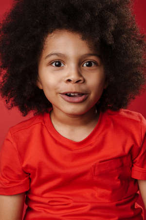 Smiling little african boy in everyday clothes over red wall background