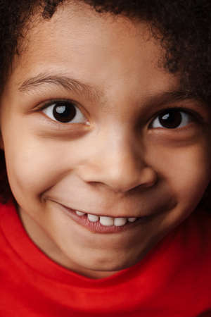 Smiling little african boy in everyday clothes over red wall background, close upの写真素材