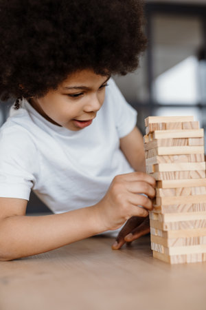 Black curly boy playing with wooden planks at homeの写真素材