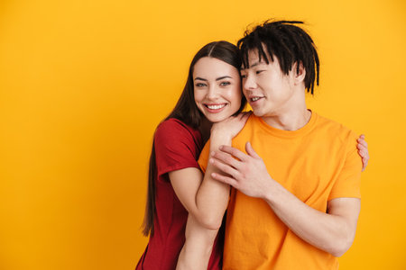 Young multiracial couple smiling and hugging while posing on camera isolated over yellow wallの写真素材