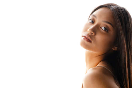 Young asian brunette woman posing and looking at camera isolated over white wallの写真素材