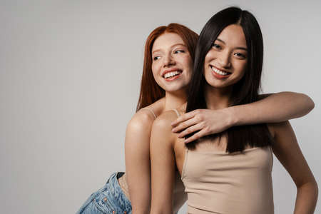 Multiracial two women hugging and laughing at camera isolated over white wallの写真素材