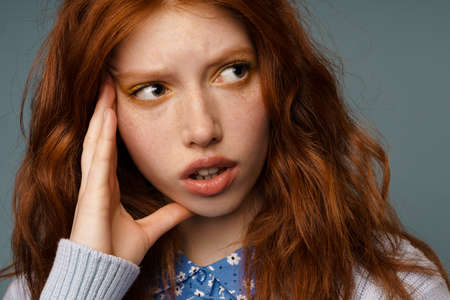 Young ginger puzzled woman thinking and looking aside isolated over grey backgroundの写真素材