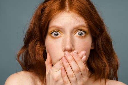 Shirtless shocked woman looking at camera and covering her mouth isolated over grey background