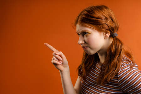 Ginger displeased woman with tails looking and pointing finger aside isolated over orange backgroundの写真素材