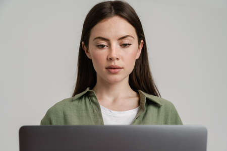 Young brunette woman in shirt posing with laptop isolated over white backgroundの写真素材
