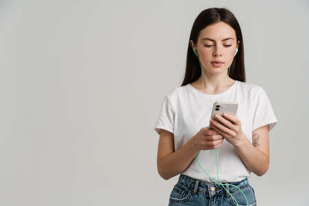 Young brunette woman listening music with earphones and cellphone isolated over white background