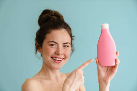Half-naked brunette woman showing and pointing finger at beauty product isolated over blue backgroundの写真素材