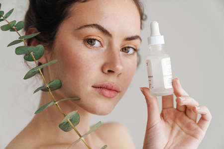 brunette woman showing face serum and eucalyptus isolated over while backgroundの写真素材