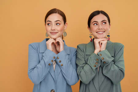 Young two women wearing jackets smiling and looking at opposite sides isolated over yellow...