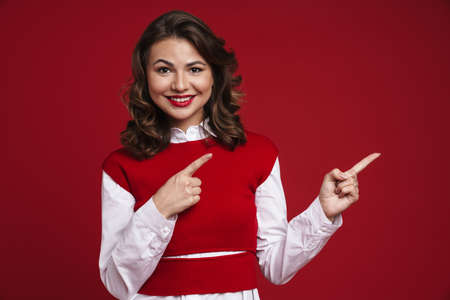 Image of a positive young woman pointing to copyspace isolated over red wall background
