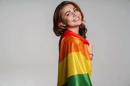 Happy beautiful woman smiling while posing with rainbow flag isolated over gray backgroundの写真素材