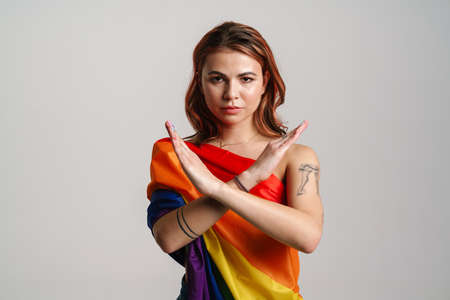 Serious woman wearing rainbow flag showing stop gesture isolated over gray backgroundの写真素材