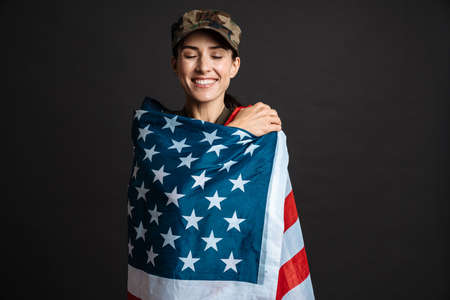 Happy soldier woman wrapped in american smiling at camera isolated over black background