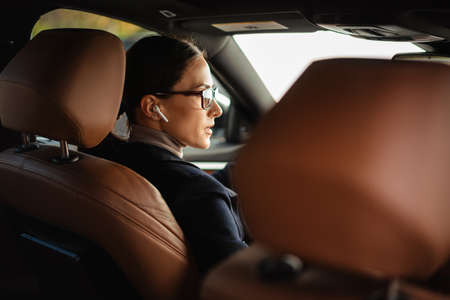 Beautiful focused businesswoman in earphones and eyeglasses driving carの写真素材