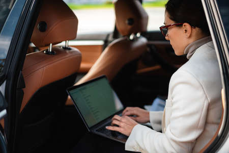 Beautiful concentrated businesswoman working with laptop while sitting in carの写真素材