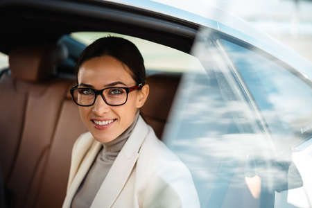 Beautiful happy businesswoman in eyeglasses smiling while sitting in carの写真素材