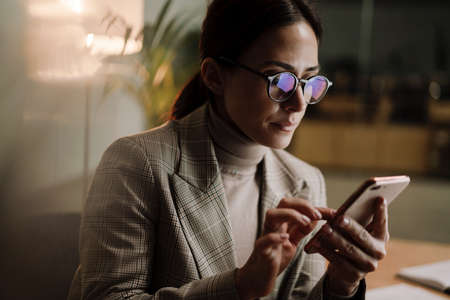 Serious charming woman using cellphone while working in officeの写真素材