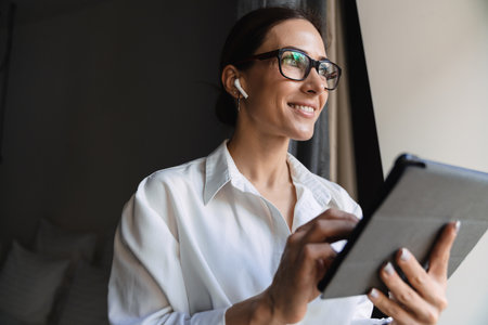 Smiling middle aged brunette white businesswoman in smart wear standing at the window in the hotel...