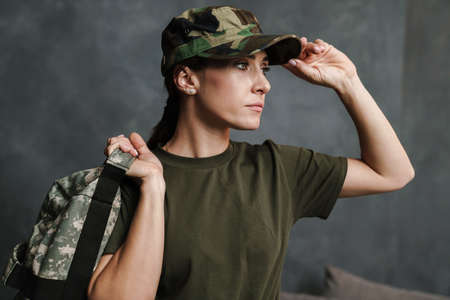 Serious beautiful soldier woman posing with bag indoors