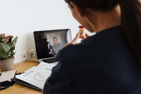 Woman doctor showing medicine while making video call on laptop at home