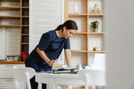 Focused woman doctor using earphone while working with laptop and papers at homeの写真素材